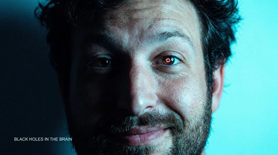 Extreme close-up of a smiling bearded man, a tiny glowing ring where one pupil should be, on a cyan background
